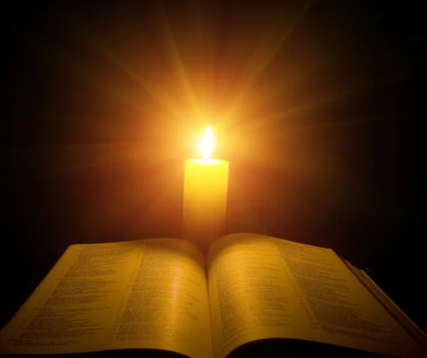 A bible open on a table next to a candle