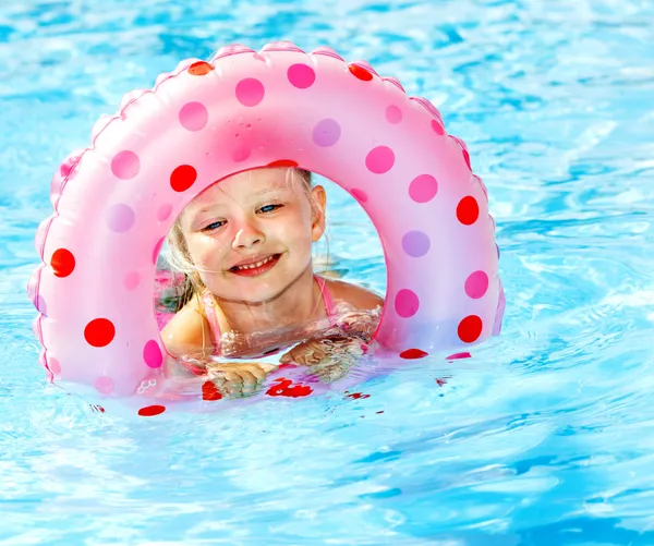 Child sitting on inflatable ring in swimming pool.