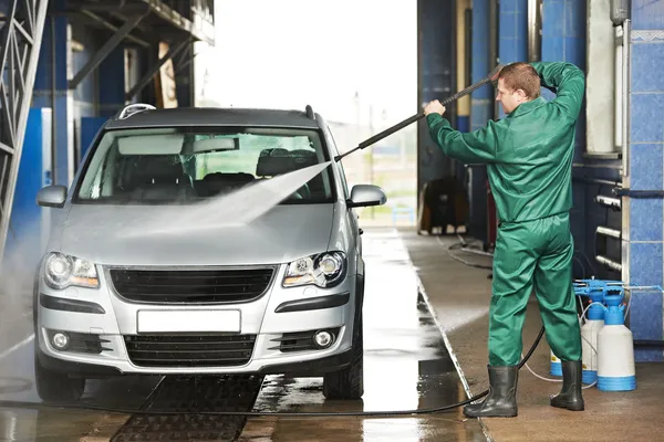 Worker cleaning car with pressured water