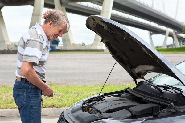Confused mature driver standing in front of vehicle with opened engine compartment hood