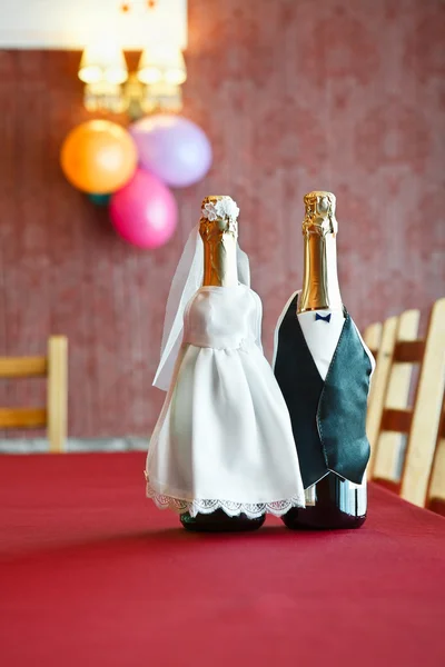 Two bottles of champagne wearing like a bride and groom standing on table.