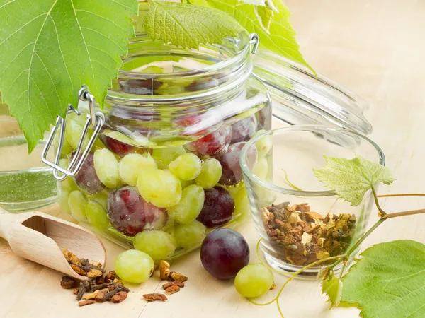 Glass jar with canned grapes, grape leaves and spice on wooden table