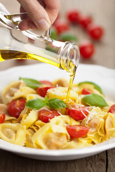 Olive oil pouring over tortellini with cheese and tomatoes