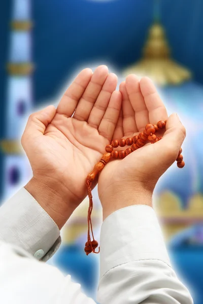 Man\'s hand holding a rosary in a pose of praying and asking