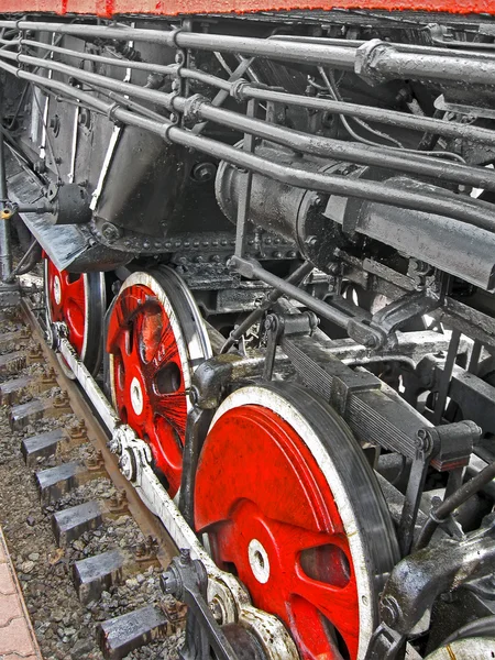 Red round steam engine wheels and metal connected pipe heap.