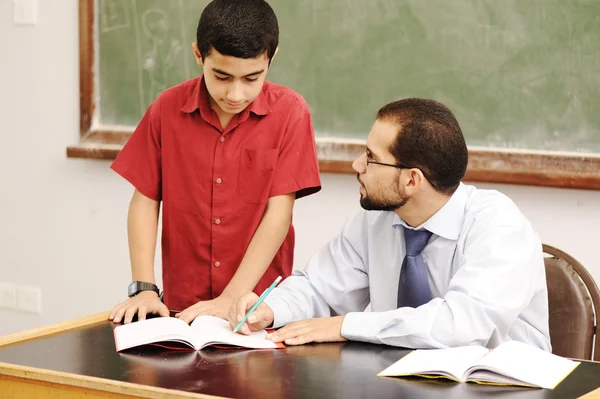 Male teacher in classroom helping a pupil in front of the board
