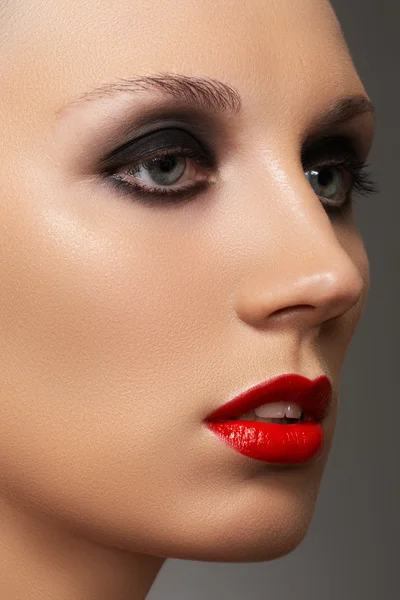 Closeup beauty portrait of attractive model face with fashion visage. Dark smoky eye makeup and bright red lips make-up