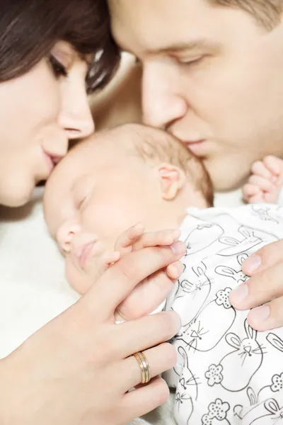 Parents holding newborn baby hand and kissing child. Family and