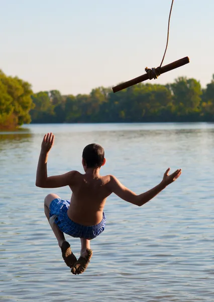 Teenage boy jumping in the river from the swinging rope on sunny summer day