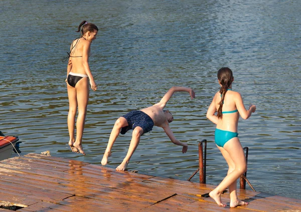Teenage boy and teenage girls jumping into the river from old dock