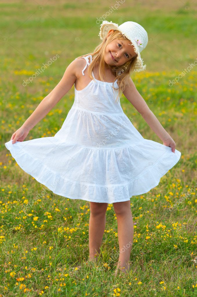 Cute little girl in white dress and hat walking on the meadow on ...