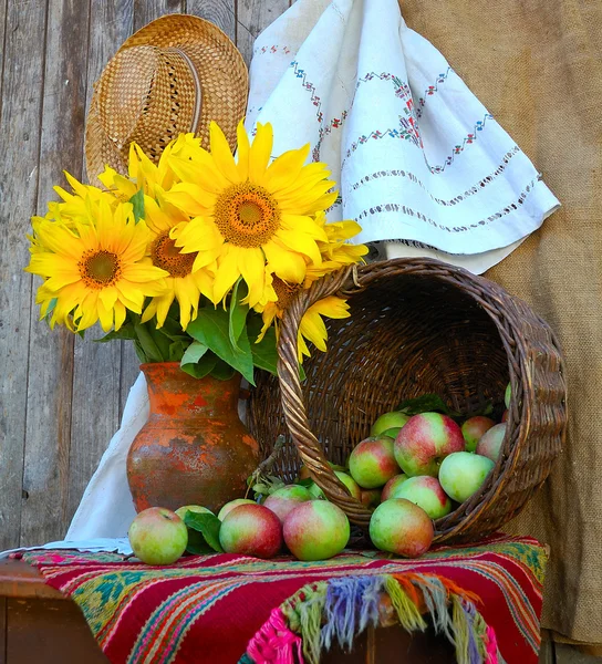 Vase with sunflowers and by a basket with apples