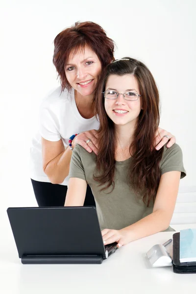 Middle aged mother help teen daughter studying computer