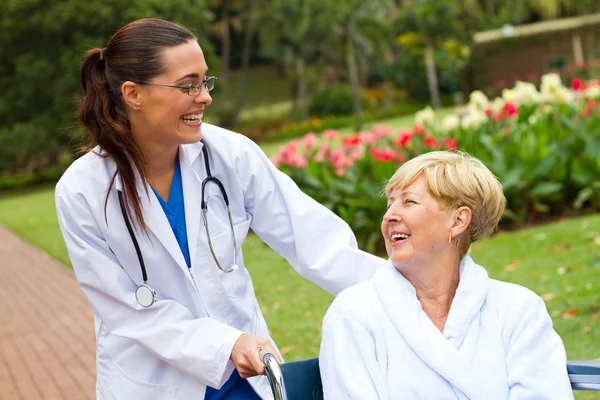 Friendly female doctor pushing senior patient in wheelchair outdoors