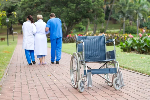 Caring doctor and nurse helping senior patient get up from wheelchair and walk