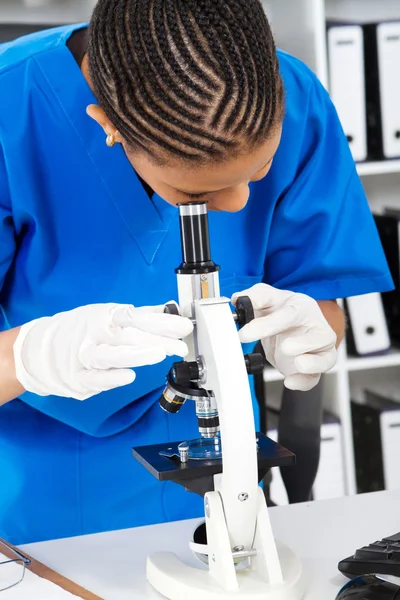 Female lab technician looking through microscope in lab