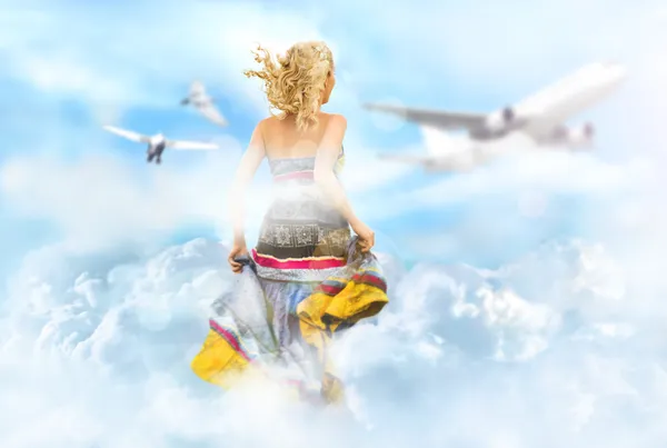 Young woman running through the clouds in the sky, birds and airplane flying at the background