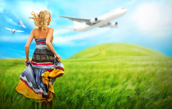 Woman running across field with idyllic landscape. Airplane and birds are flying in the sky