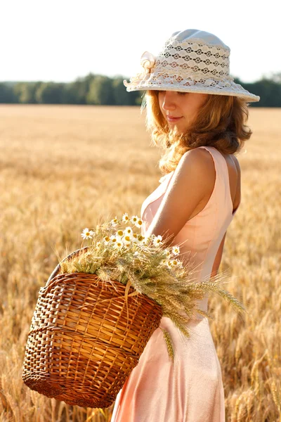 Beautiful woman with basket full of ripe spikelets of wheat in the field