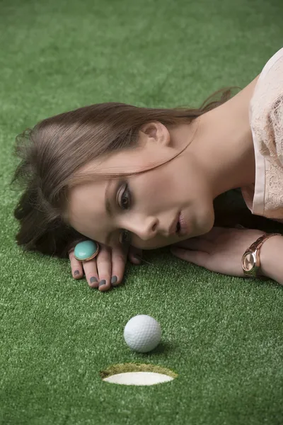 Girl lying on grass with golf ball, she hits