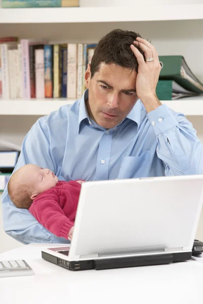 Stressed Father With Newborn Baby Working From Home Using Laptop
