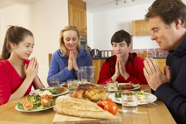 teenage family saying grace before eating lunch together in kitc