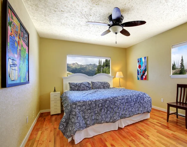 Small bedroom with yellow walls, mountain view and grey bed.