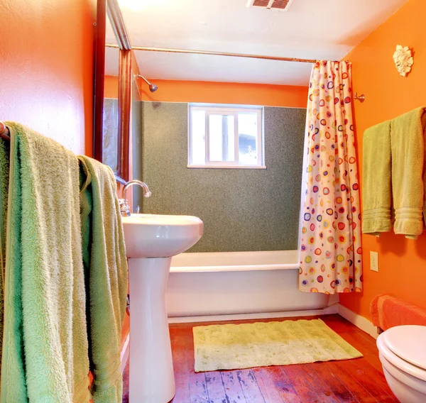 Orange and green bathroom with tub and wood floor.