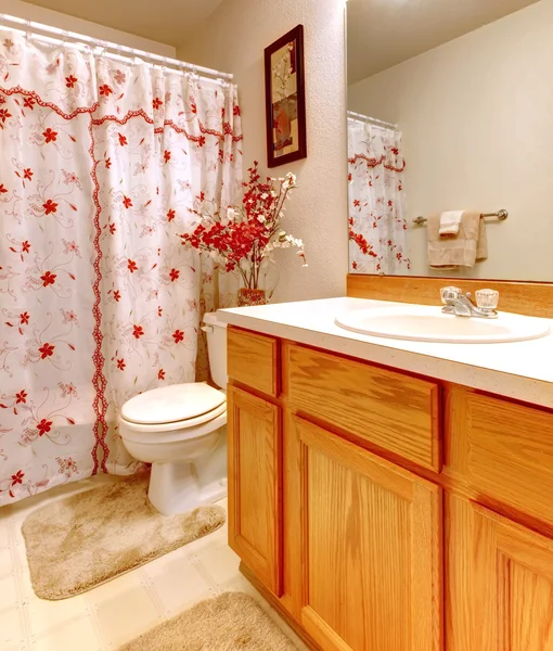 Simple bathroom with flowery shower curtain and wood cabinet.