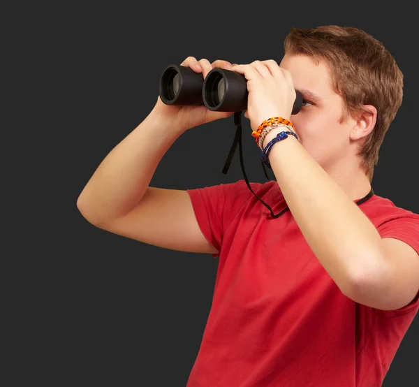 Portrait of young man looking through a binoculars over black ba