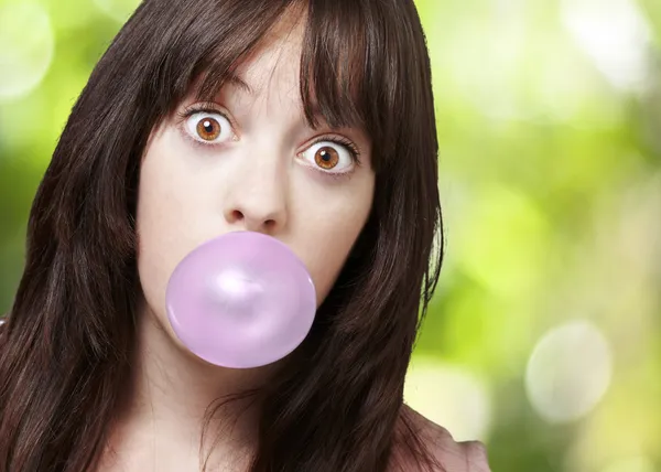 Young girl with a pink bubble of chewing gum against a nature ba