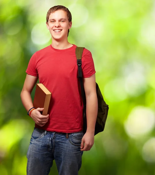Portrait of young student holding book and carrying backpack aga