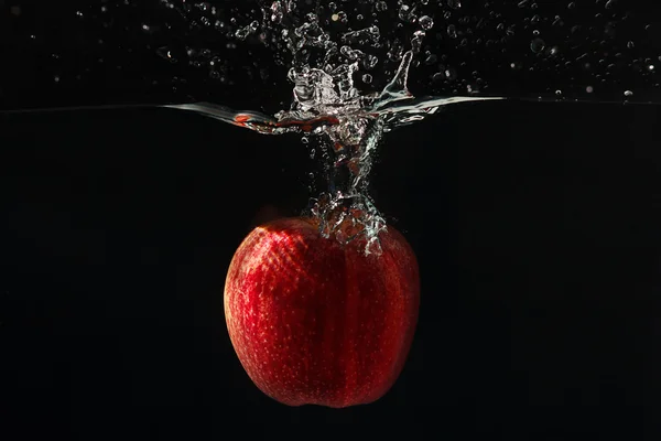 Red apple falling into the water with a splash on a black background