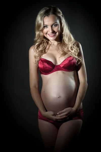 Beautiful pregnant blond woman in red lingerie holding her belly