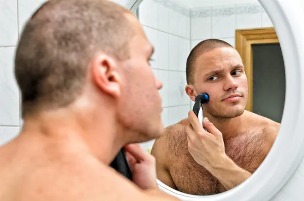 Male shaving in bathroom in front of the mirror.