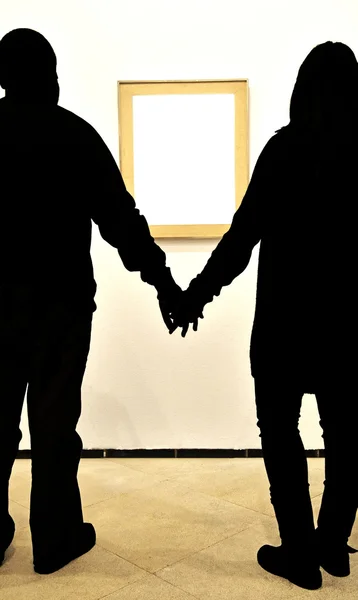 Silhouette of couple holding hands looking white box into a museum