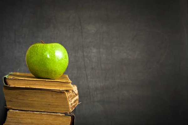 Green apple on old book against blackboard
