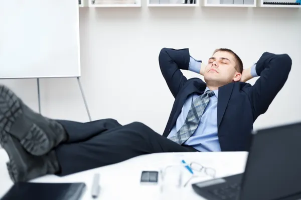 Tired businessman sleeping on chair in office with his legs on t