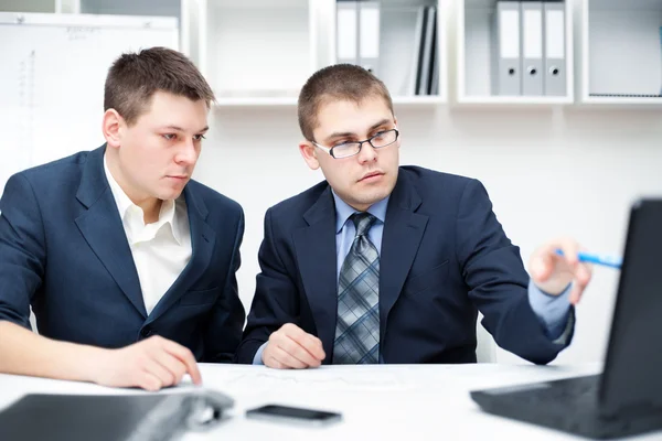 Two young businessmen working together with computer at office d