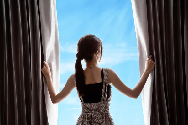 Young woman opening curtains and blue sky