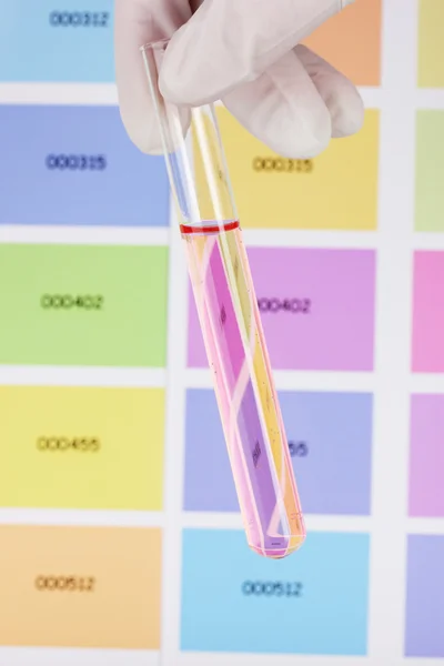 Tube with pink liquid in hand on color samples background