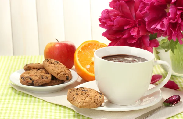 Cup hot chocolate, apple, orange, cookies and flowers on table in cafe