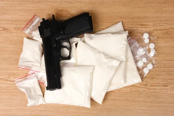 Cocaine and marihuana in packages and handgun on wooden background