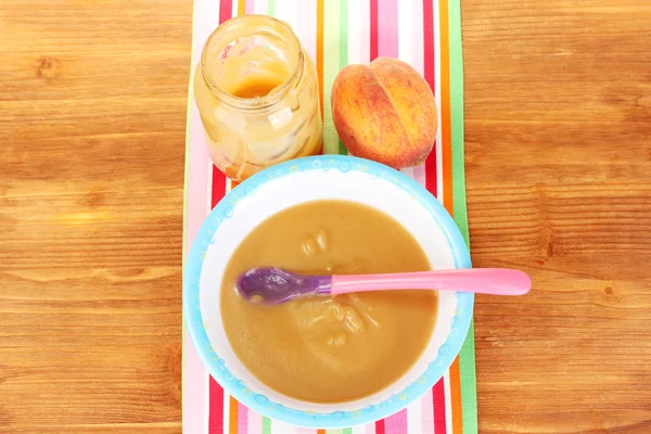 Peach baby food in a plate on colorful napkin on wooden table close-up