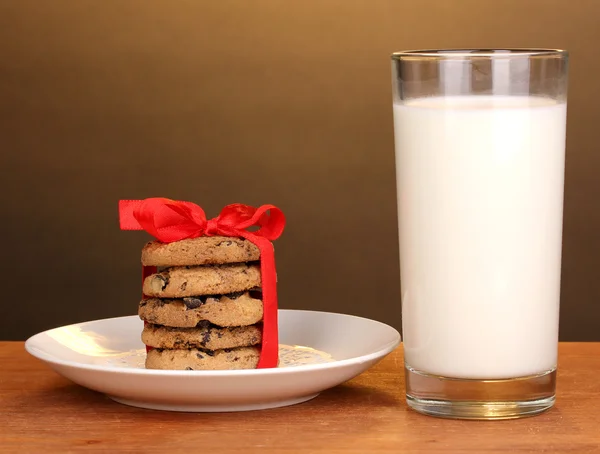 Glass of milk and cookies on wooden table on brown background