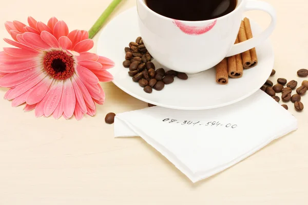 Cup of coffee with lipstick mark and gerbera beans, cinnamon sticks on wooden table
