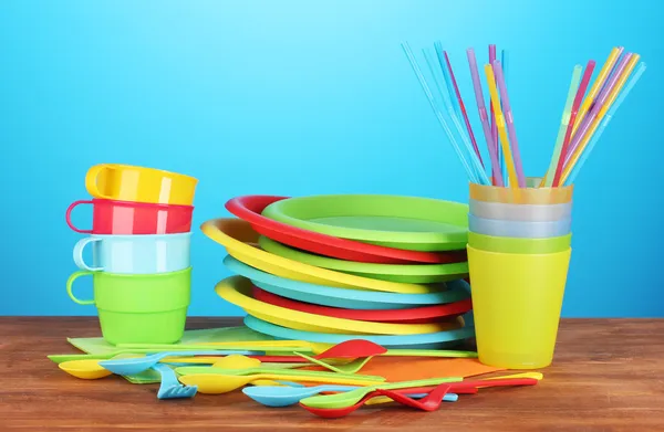 Bright plastic disposable tableware on wooden table on colorful background
