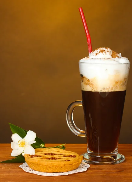 Glass of coffee cocktail with tart on doily and flower on brown background