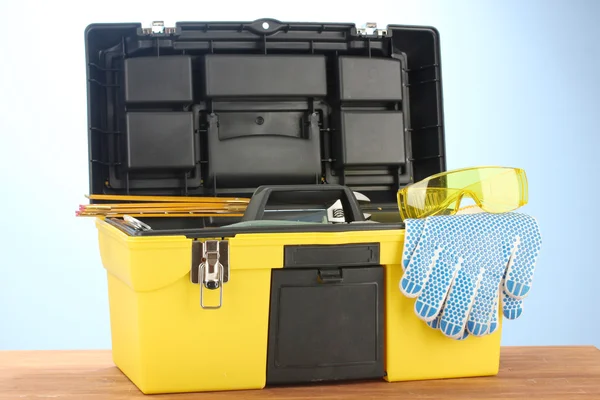 Open yellow tool box with tools on blue background close-up