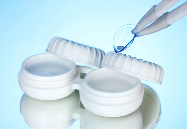 Contact lenses in containers and tweezers on blue background